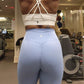 Woman at the gym posing in active-wear brand Sweat or Sparkle Athletics White Cross-Back Sports Bra paired with Carolina Blue Scrunch Leggings.